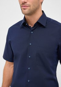 Kurzärmliges navyblaues Hemd mit Button-Down-Kragen, strukturierter Stoff, Brusttasche und kontrastierenden blauen Knopfakzenten.