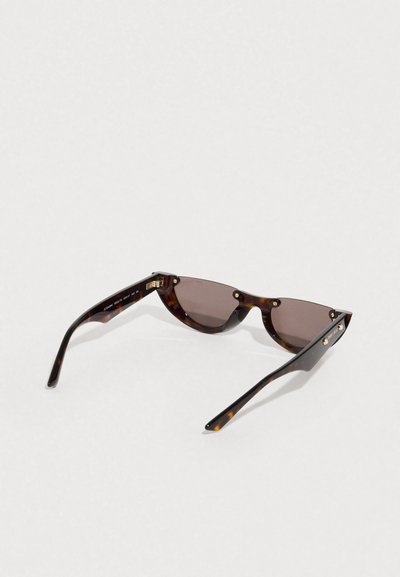 Γυαλιά ηλίου με καφέ θολό φακό, γκρι φακούς με γωνίες, μεταλλικά στοιχεία σε χρυσό τόνο και καμπυλωτούς μαύρους βραχίονες.