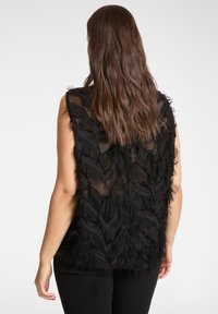 Top nero senza maniche con dettagli a frange testurizzate, schiena in tessuto trasparente e vestibilità ampia. Dettagli includono frange stratificate e ondulate.