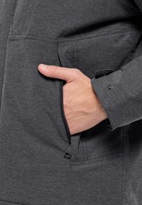 Giacca grigia con tasca con zip, texture liscia e polsini con bottone, che mostra un design pratico per l'uso quotidiano.
