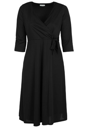 Woman wearing a black, knee-length dress with three-quarter sleeves and red high-heeled ankle boots, standing with back facing the viewer.