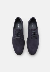 Chaussures en daim bleu marine avec une texture lisse, bout rond et lacets. Elles possèdent une semelle en caoutchouc plate et des accents cousus sur les côtés.