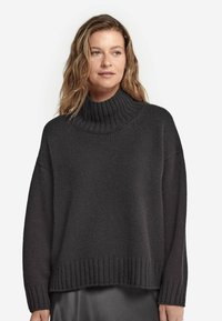 Kolgrå tröja med ribbad polokrage, lös passform och sänkta axlar. Texturen är mjuk, stickad tyg med rak nederkant.