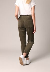 Olijfgroene corduroybroek met een hoge taille, zijzakken en achterzakken, gecombineerd met een wit t-shirt en witte sneakers.