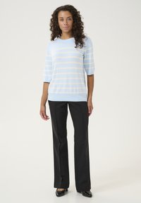 Heledsinine sviiter, millel on kreemjad horisontaalsed triibud, lühikeste varrukatega, paari pandud mustade kohandatud pükste ja mustade kontsadega. Sile tekstuur, juhuslik sobivus.