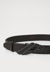 Cinturón de cuero negro con una hebilla texturizada que presenta la marca "ICON" en relieve. Correa ajustable con un acabado suave y un diseño minimalista.