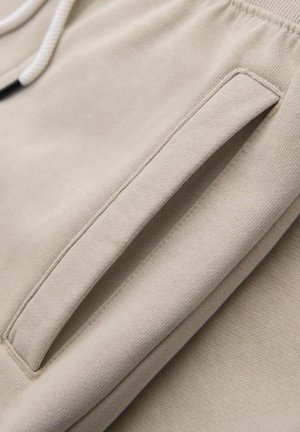 Pantalones de chándal beige con una suave textura, un bolsillo lateral con una sutil abertura y cordón en contraste.