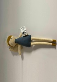 Stuffed doll with a beige face, brown hair, and white wings. It wears a dark blue dress and has long limbs with brown shoes. Care tag visible.