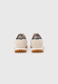 Paire de baskets crème et beige avec semelles marron, vues de dos, présentant des panneaux de talon noirs pailletés avec la marque "Blauer".