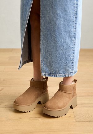 Bottes cheville en daim marron avec une semelle plateforme beige épaisse, dotées d'un bas de cheville bas et d'une doublure intérieure douce, associées à une jupe en jean.