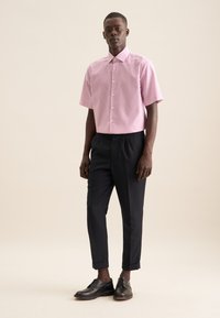 Camicia a maniche corte con bottoni, a righe verticali rosa e bianche, abbinata a pantaloni scuri affusolati e scarpe nere stringate.