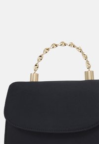 Černá kabelka s hladkou texturou, opatřená zkroucenou zlatou rukojetí a kovovými akcenty. Design zahrnuje klopové zapínání.