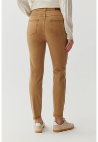 Jeans ajustados beige con una textura suave y bolsillos traseros, combinados con zapatillas beige con acentos blancos y suela de goma.