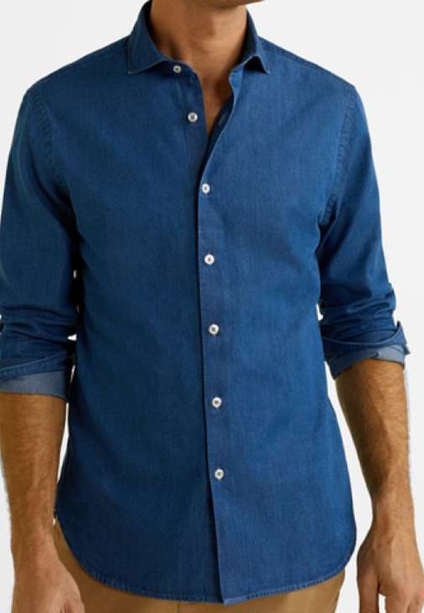 Homme portant une chemise cintrée bleu foncé à manches longues avec les manches retroussées, associée à un pantalon marron clair.