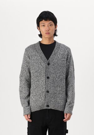 Cardigan grigio a maglia con scollo a V, sette bottoni lungo la parte anteriore, polsini a costine e un motivo testurizzato. Indossato sopra una maglietta nera.