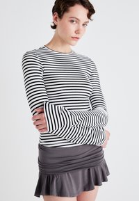 Black and white striped long-sleeve shirt with flared cuffs, paired with a gray ruffled mini skirt. Smooth fabric texture, fitted design.