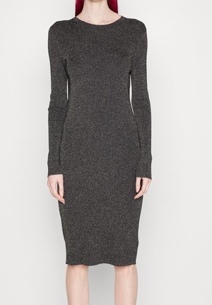 Vrouw draagt een nauwsluitende, lange mouw, knielange donkergrijze gebreide jurk met subtiele glans, staand tegen een effen witte achtergrond.