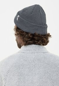 Gorra de punto gris con un diseño acanalado, combinada con una chaqueta de forro polar texturizado gris claro, vista desde la parte de atrás.