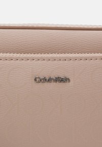 Portafoglio beige testurizzato Calvin Klein con logo argentato, tasca zip orizzontale, superficie liscia e motivo goffrato sottile.