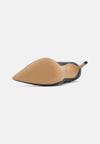 Chaussure noire à bout pointu avec une tige texturée et une semelle en caoutchouc lisse marron clair dotée de rainures horizontales pour une meilleure adhérence.