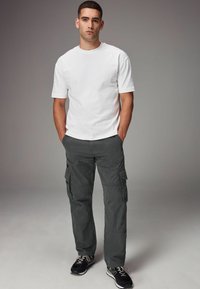 Hvid bomulds t-shirt parret med grå cargo-bukser med flere lommer. Modellen afslutter looket med sorte sneakers.