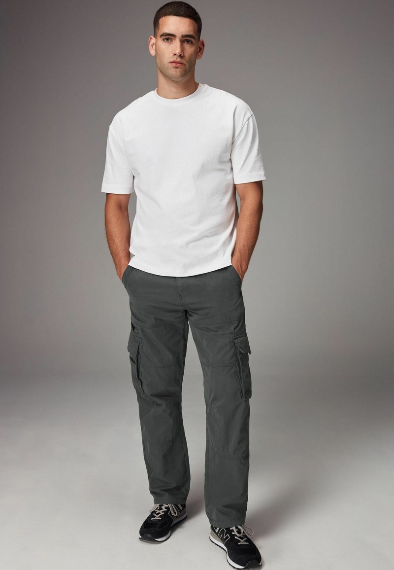 Hvid bomulds t-shirt parret med grå cargo-bukser med flere lommer. Modellen afslutter looket med sorte sneakers.