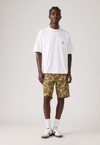 White short-sleeve t-shirt with a chest pocket, paired with green camo shorts. Model wears white socks and sneakers with black accents.