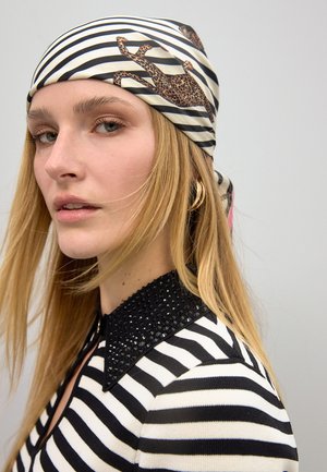 Bufanda a rayas blancas y negras con un acento de estampado de leopardo, hecha de una tela suave. El modelo lleva una blusa con collar de cuentas negras.