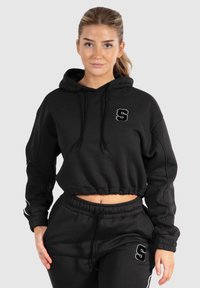 Schwarze, gekürzte Kapuzenjacke mit Fronttasche, Kordelzugkapuze und gesticktem "S"-Logo. Dazu passende schwarze Jogginghosen. Weicher Stoff.