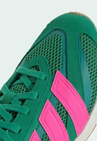 Zelené tenisky s sieťovinou, semišovými akcentmi a ružovými pruhmi. Disponujú textúrovaným povrchom a gumovou podrážkou pre lepšiu priľnavosť.