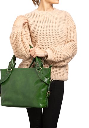Grüne Leder-Shopper-Tasche mit doppelten Griffen und Metallakzenten, kombiniert mit einem hellbeigen, strukturierten Strickpullover und schwarzen Slim-Fit-Jeans.