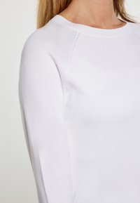 Weißer Baumwollmischpullover mit Rundhalsausschnitt, langen Raglanärmeln und glatter Textur mit dezenten Steppdetails.