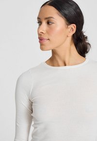 Top bianco a maniche lunghe con scollatura rotonda. Design leggero e aderente che mette in risalto la forma del corpo, con una texture sottile.