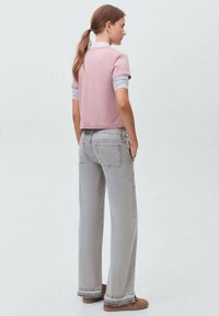 Cropped top rosa corto con maniche a strisce grigie; jeans grigi a vita alta, larghi, con orli sfrangiati; modella di spalle, scarpe casual marroni.