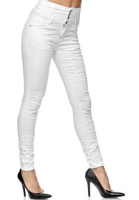 Jeans ajustados de talle alto blancos con un acabado texturizado, que presentan un cierre de botón y una silueta ajustada, combinados con zapatos de tacón negros.