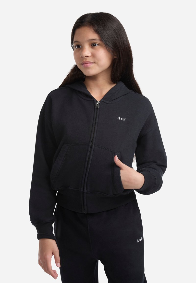 Sudadera negra con cremallera, hecha de tejido suave, que cuenta con un bolsillo frontal, puños acanalados y un pequeño logo bordado en el pecho.