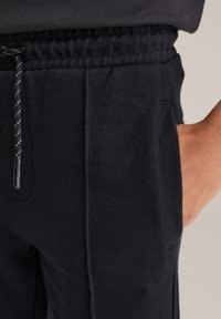 Svarta mjukisbyxor i ett mjukt, strukturerat tyg. Har en elastisk midja med dragsko och sidofickor.