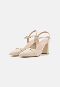 Beige högklackade skor med spetsig tå, ankelrem med spänne och blockklack; slät lädermaterial med matt yta.