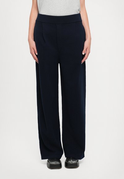 Pantalons larges bleu marine avec une taille côtelée et des plis avant, faits d'un tissu doux. Associés à des chaussures plates noires.