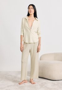 Világos bézs színű, kényelmes otthoni viselet szett, amely egy galléros, gombos ingből és laza szabású nadrágból áll, puha, texturált anyagból készült.