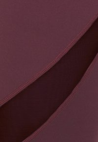 Närbild av vinröd tyg med ett diagonalt nätpanel och sydda sömmar längs kanterna.