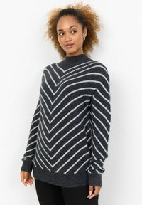 Pull en tricot gris foncé avec des rayures en chevron blanches, présentant un col montant et des manches longues. Texture douce et coupe décontractée.