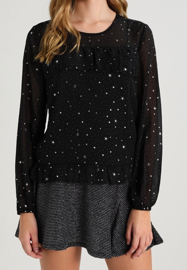 Haut noir transparent à manches longues avec motif d'étoiles, encolure à volants et corsage ajusté, associé à une jupe métallique texturée à ourlet évasé.
