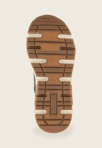 Semelle de chaussure en caoutchouc avec une surface texturée marron, dotée d'accents de bande blanche et d'une étiquette de logo centrale. Forme ovale avec des rainures bien définies.