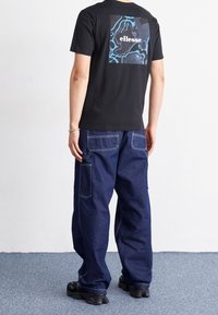 Černé bavlněné tričko s modrošedou grafikou na zadní straně, kombinované s volnými tmavě modrými džíny s nášivkovými kapsami.