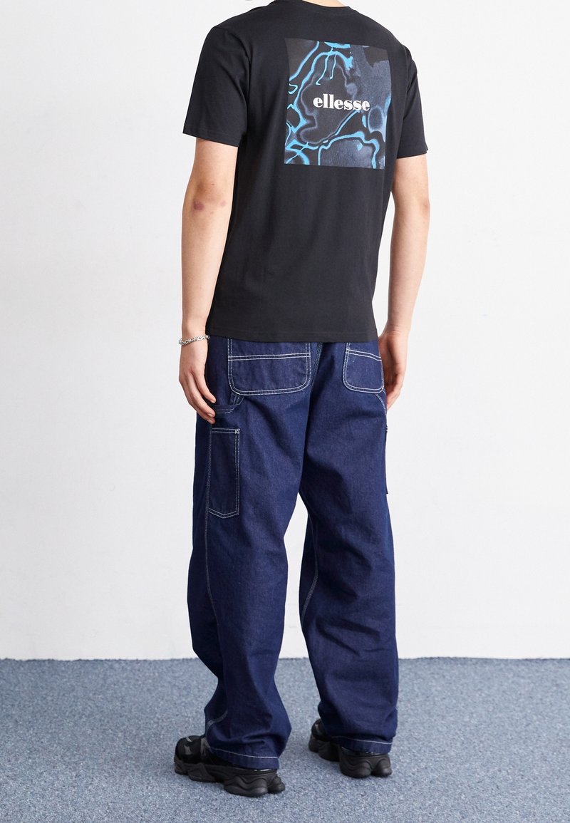 Černé bavlněné tričko s modrošedou grafikou na zadní straně, kombinované s volnými tmavě modrými džíny s nášivkovými kapsami.