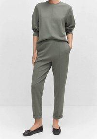 Felpa verde oliva e pantaloni tapered abbinati in tessuto liscio. I pantaloni sono arrotolati alle caviglie; abbinati a scarpe basse nere.