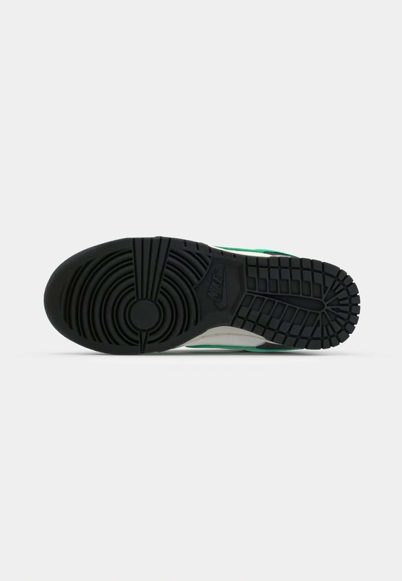 Semelle de sneaker en caoutchouc noir avec un motif de bande de roulement circulaire et des sections texturées. Présente des accents verts, blancs et noirs le long des bords.