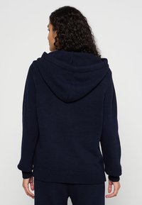 Dunkelblaues Strick-Hoodie mit lässiger Passform, ausgestattet mit einer großen Kapuze, gerippten Bündchen und Saum, strukturiertem Material und ohne sichtbare Logos.