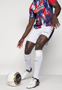 Fotbalový dres Nike s červeným, bílým a modrým grafickým vzorem, na kterém je nápis "Qatar Airways". Bílé kraťasy, bílé ponožky a černý a zlatý fotbal.